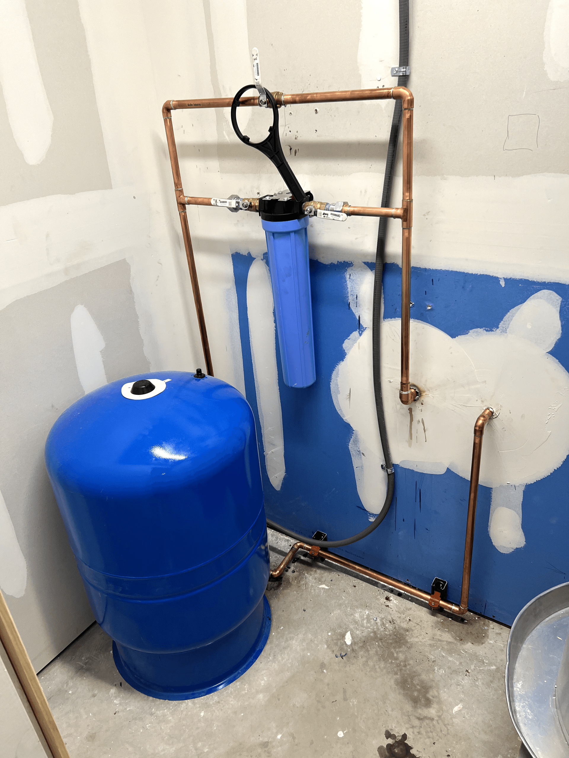 A blue tank is sitting next to a copper pipe in a room.