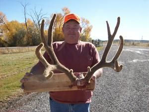 Man holding large deer antlers, outside on a road, wearing an orange hat.