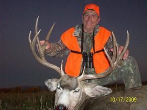 Hunter in orange vest kneels next to large buck with impressive antlers on October 17, 2009.