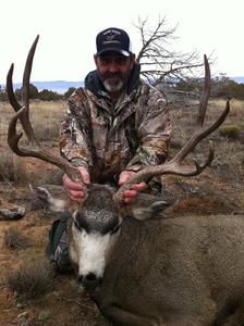 Man in camouflage holds up large deer antlers in a field.