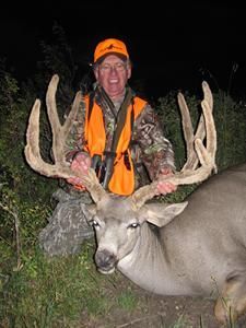 Hunter in orange vest holding large deer antlers, night setting.