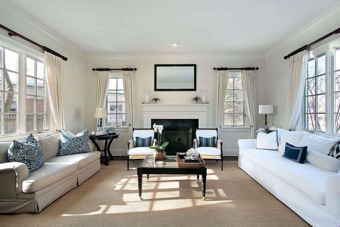 Bright living room with white sofas, coffee table, fireplace, and large windows with patterned curtains