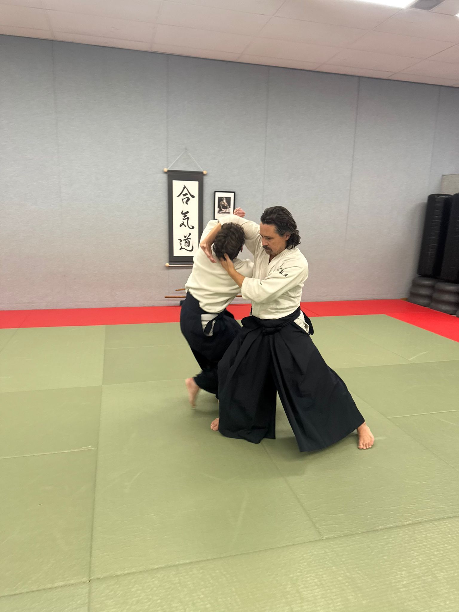 Twee mensen oefenen Aikido op een mat. De ene persoon houdt de ander vast bij het hoofd.