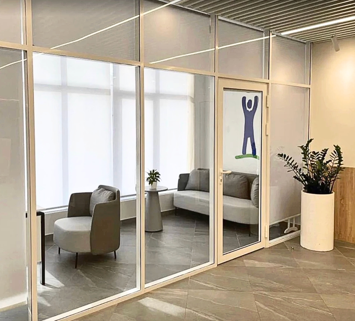 Waiting room with frosted glass walls, gray seating, and a door with a person-shaped graphic.