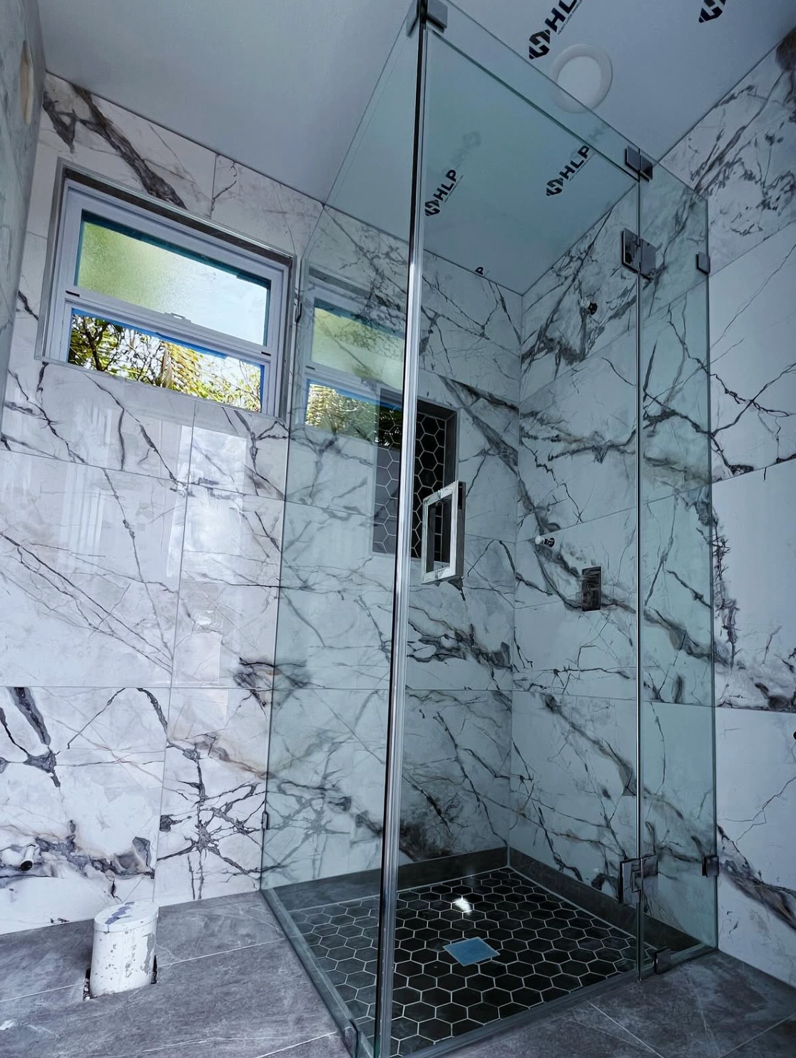 Modern bathroom with marble walls, glass shower, and small window.