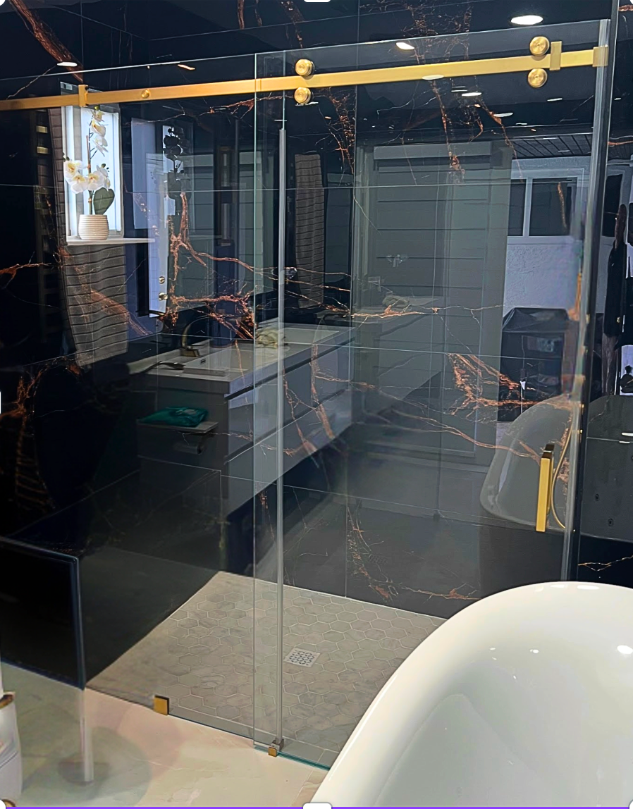 Bathroom with black and gold marble walls, glass shower door, and white bathtub.