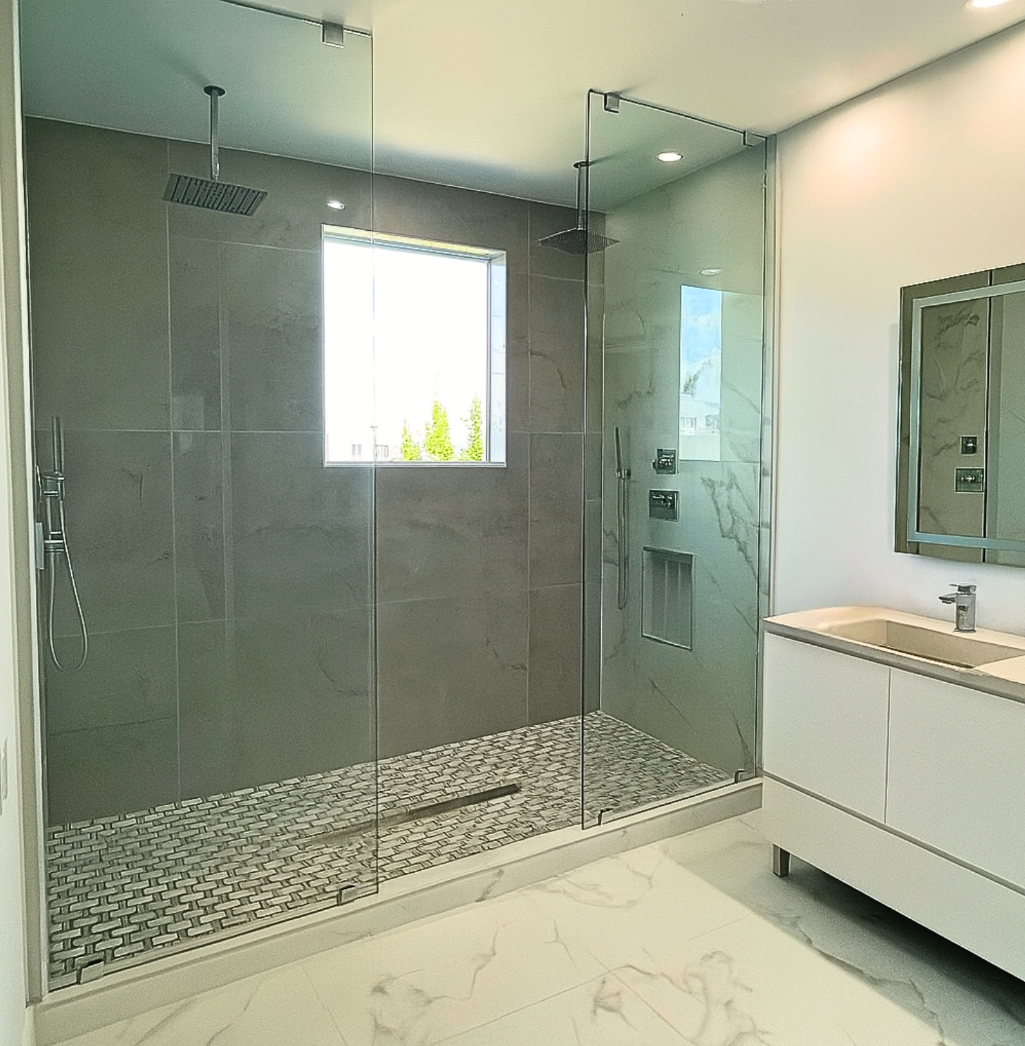 Modern bathroom with glass shower, gray tile wall, pebble shower floor, white vanity.