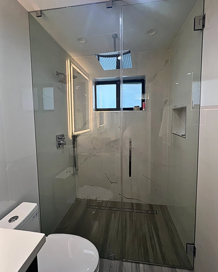 Glass-enclosed shower with a gray-tiled floor, a window, and a white toilet.