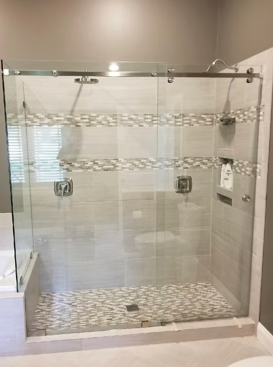 Glass shower enclosure with sliding door, pebble tile floor, and decorative tile accents.