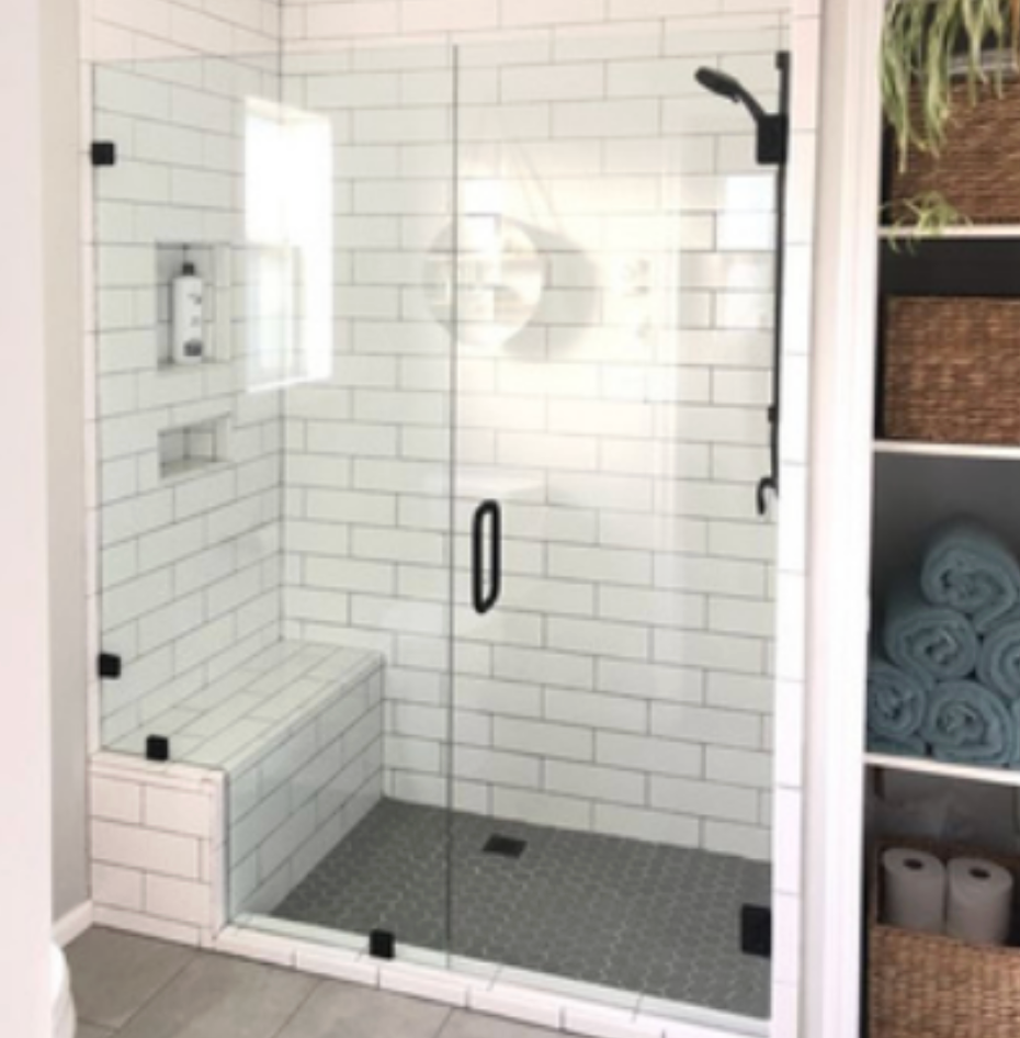 Modern white-tiled shower with glass door, black fixtures, and built-in bench. Dark gray tiled floor.