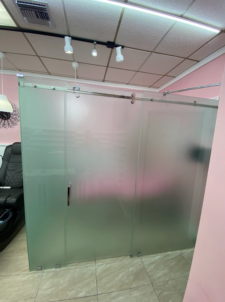 Frosted glass door and walls, with a black massage chair on the left. Pink walls and a tiled floor.