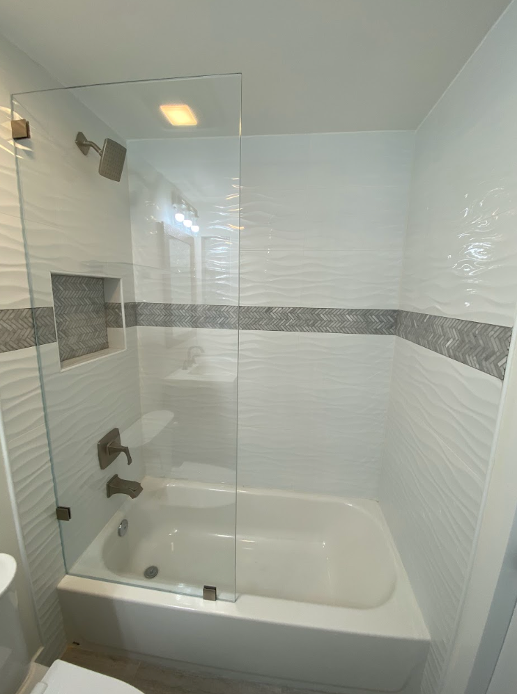 White bathroom with tub, glass shower screen, and textured tile.