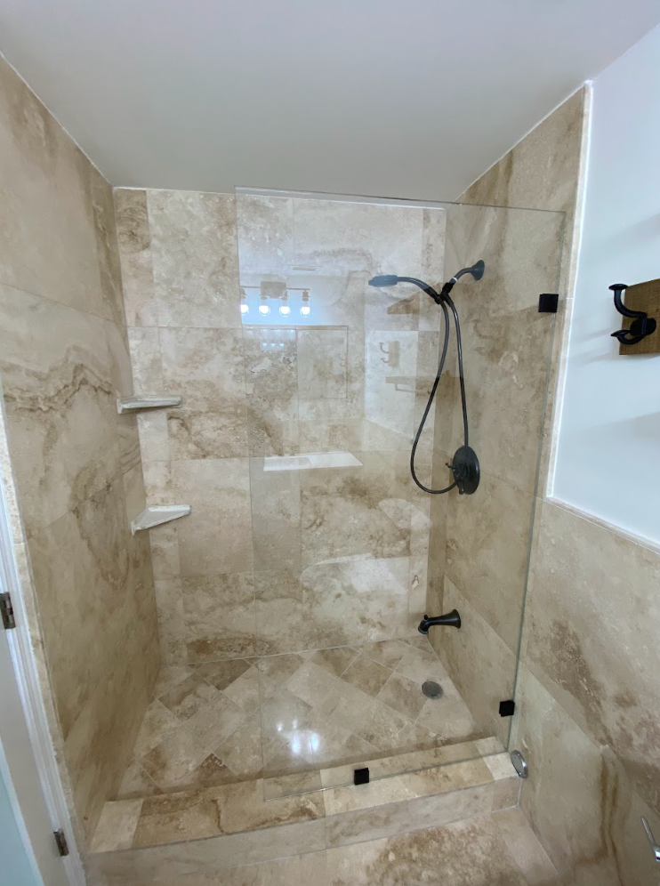 Shower with light beige tile, glass doors, and black hardware.