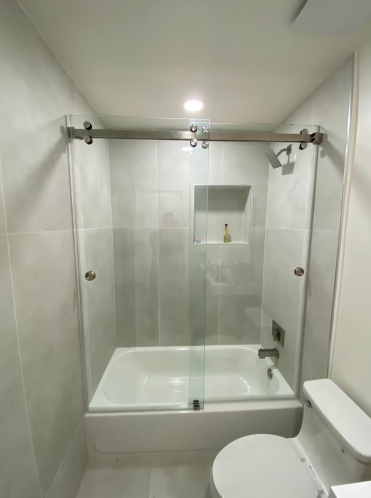 Bathroom with a white bathtub, gray tile walls, and a glass sliding shower door.