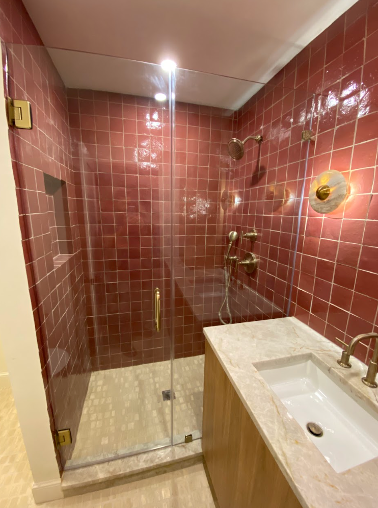 Red-tiled shower with a glass door, gold fixtures, and a marble vanity in a modern bathroom.