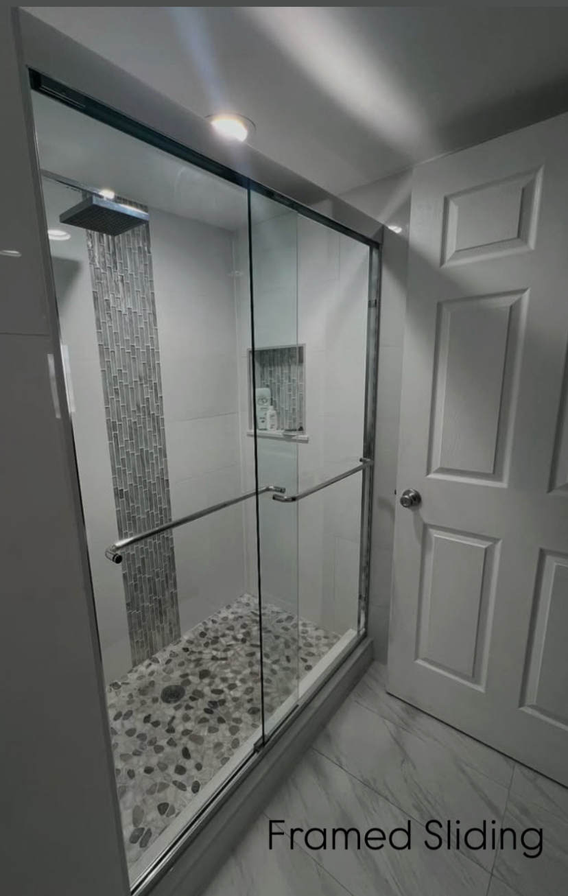 Framed sliding glass shower door in a modern bathroom. Gray pebble flooring and mosaic accent wall.