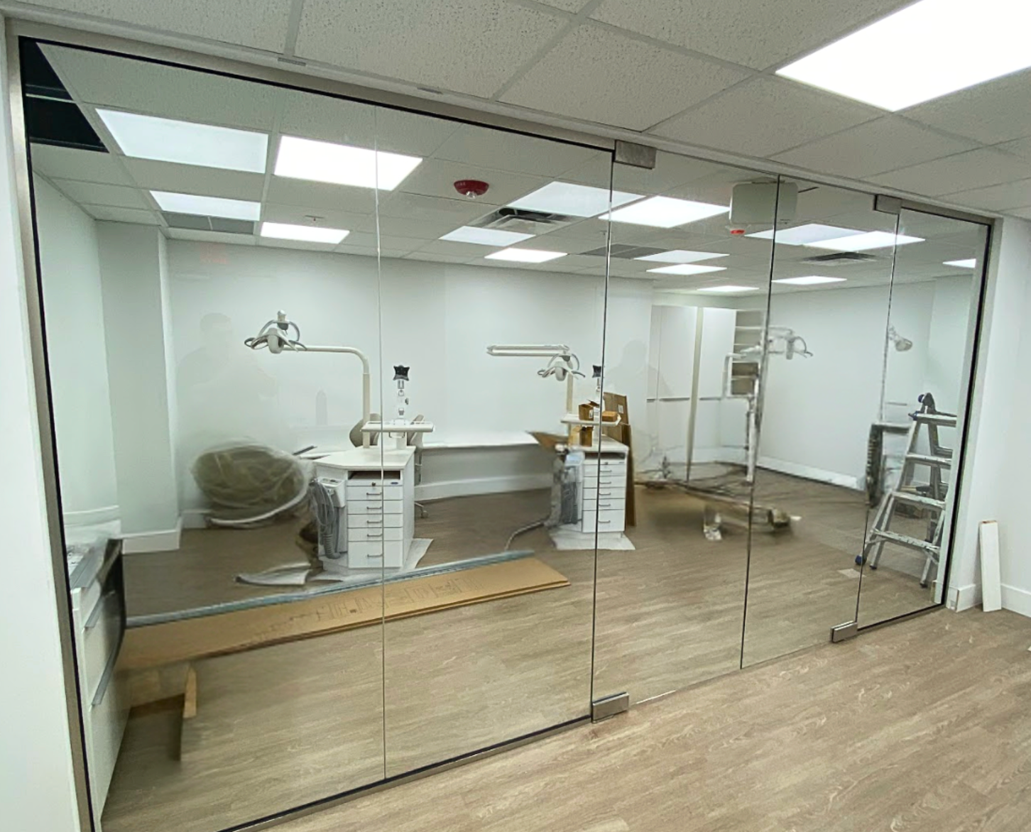 Glass-walled dental office interior with chairs, equipment, and a ladder, reflecting the room.