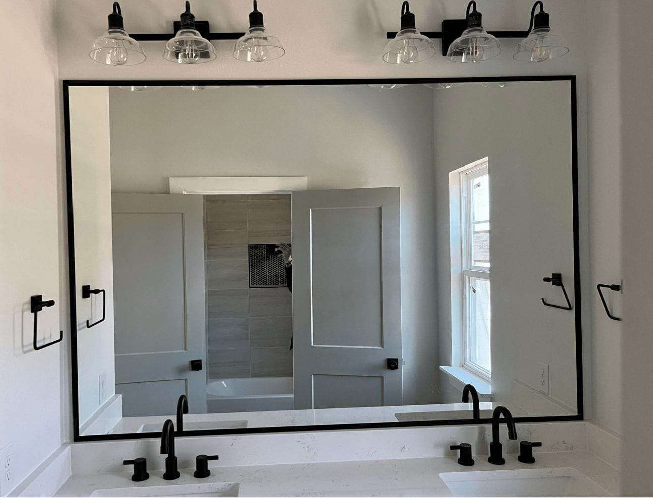 Bathroom mirror with frame, marble sink and farmhouse light fixtures.