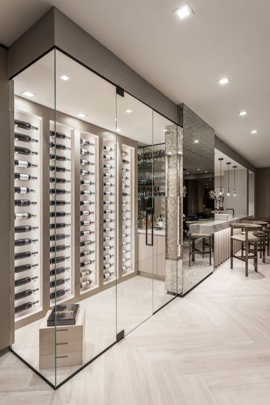 Modern wine cellar with glass walls displaying rows of wine bottles; adjacent bar area with seating.
