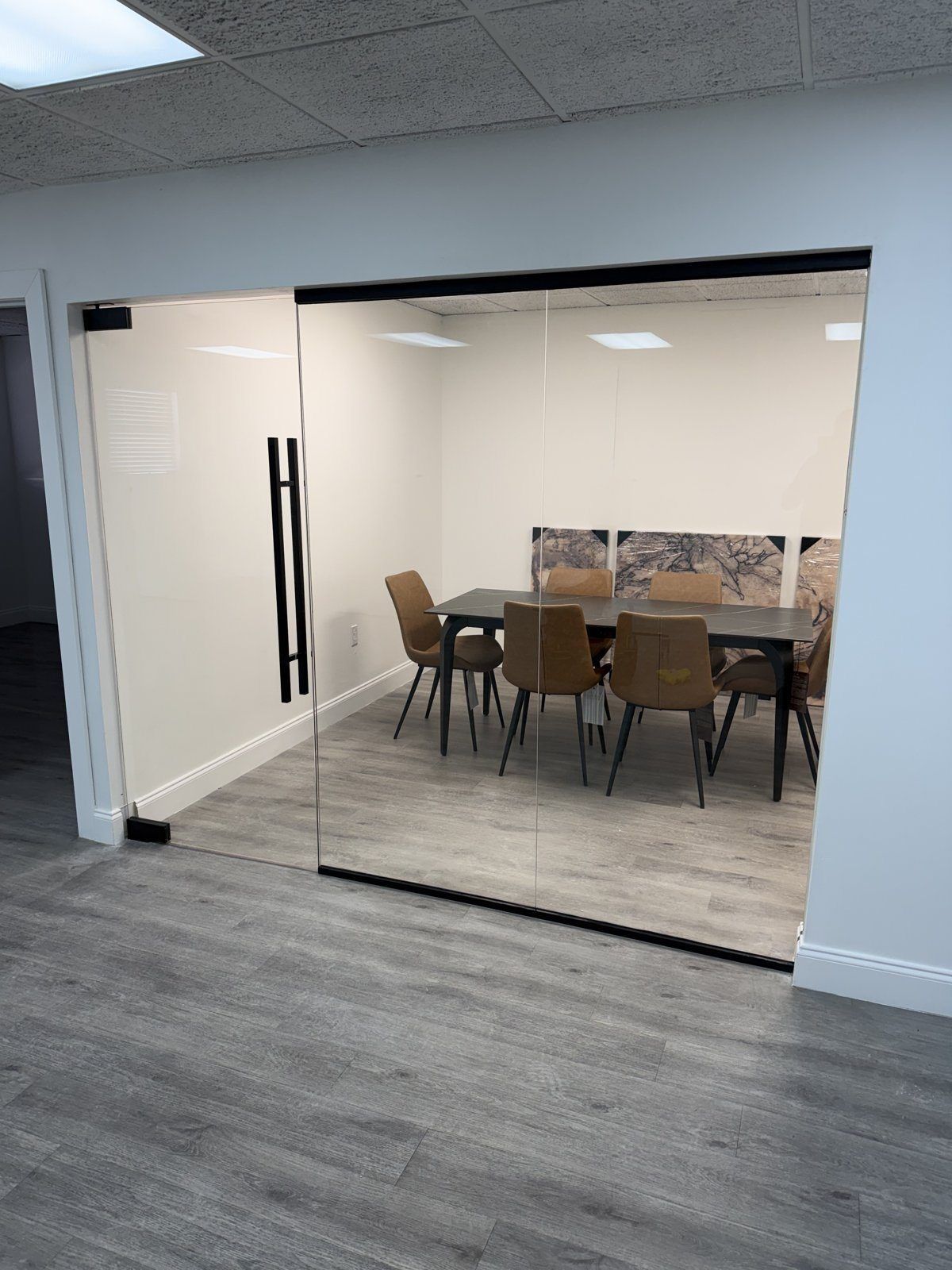 Sala de conferencias con pared de vidrio transparente sin marco, canales negros y puerta abatible de vidrio sin marco con tirador tipo escalera negro largo, Miami