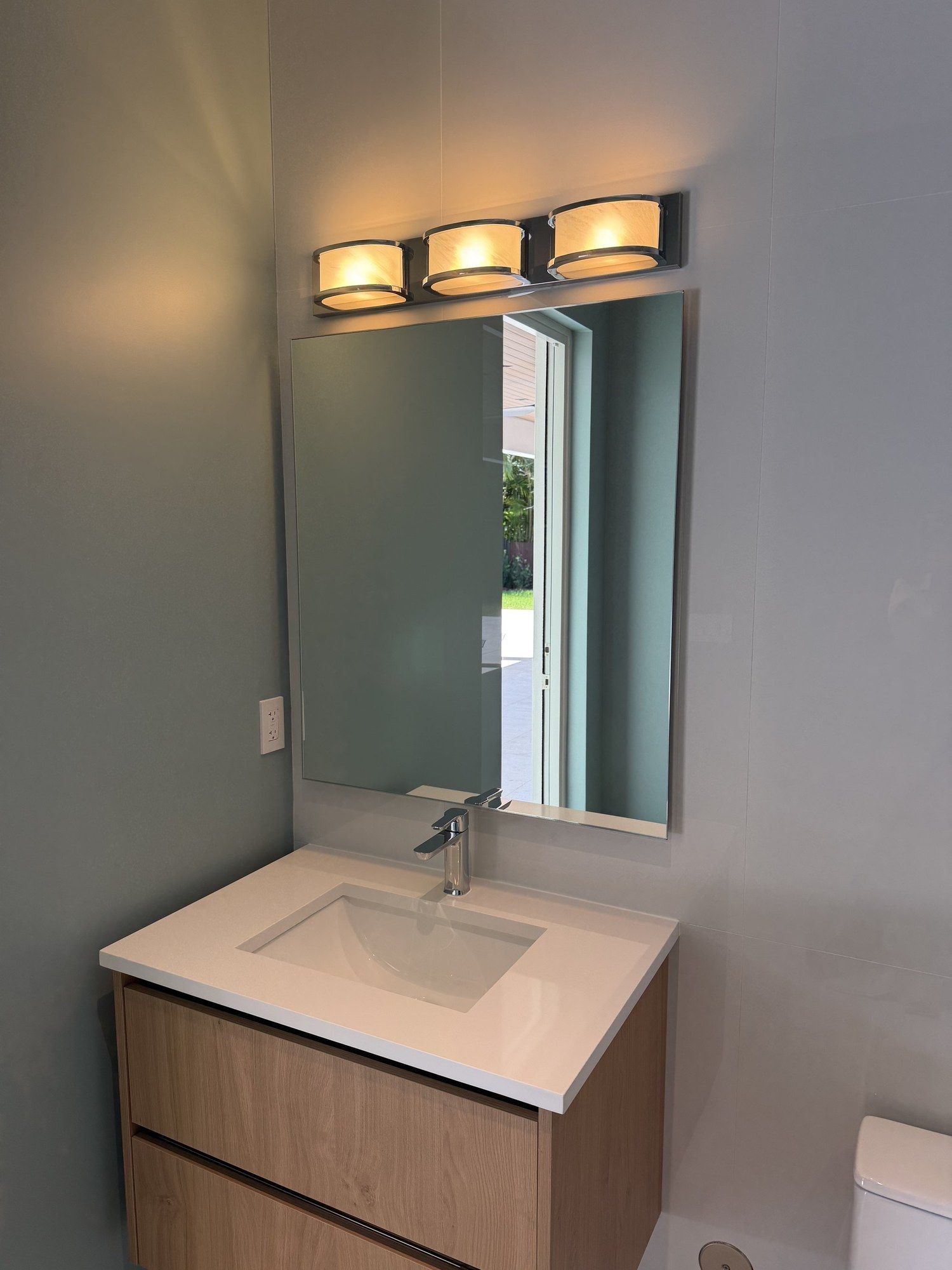Mirror with internal lighting, mounted on ribbed wall above a dark sink and gold faucet.