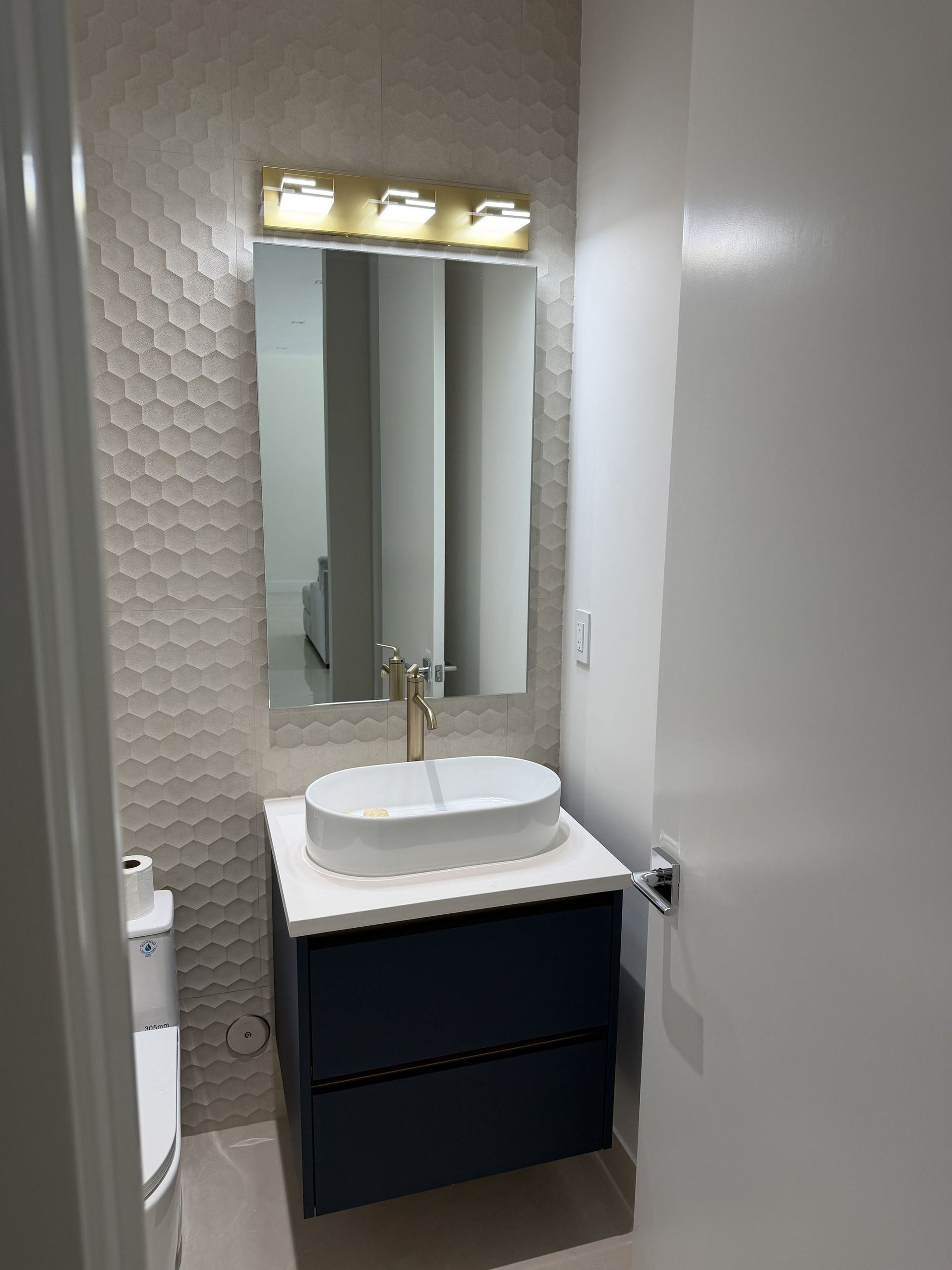 Frameless bathroom mirror above a navy vanity with vessel sink in Miami