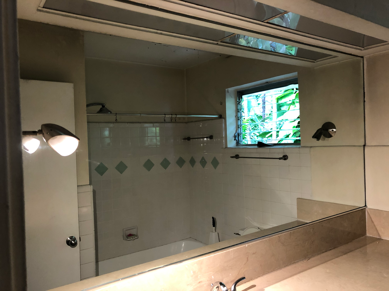 Bathroom with a large mirror reflecting a bathtub, small window with foliage, and overhead lighting.