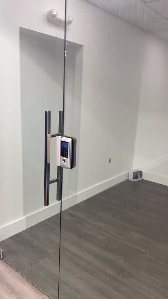 Glass door with silver handle and key card reader. Gray floor, white walls.