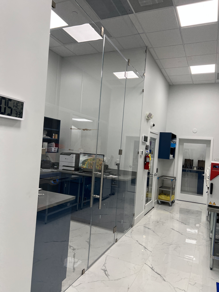 Office interior with glass doors, white walls, and a view of a workspace.