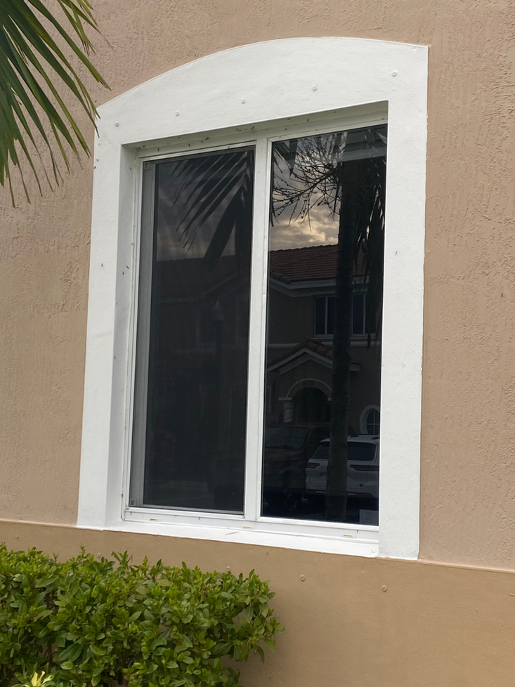 White-framed window with a rounded top on a tan wall. Green bushes are at the base.