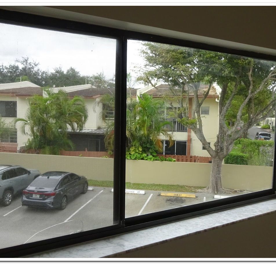 View through a window, looking at a parking lot with cars and a tree-lined residential area.