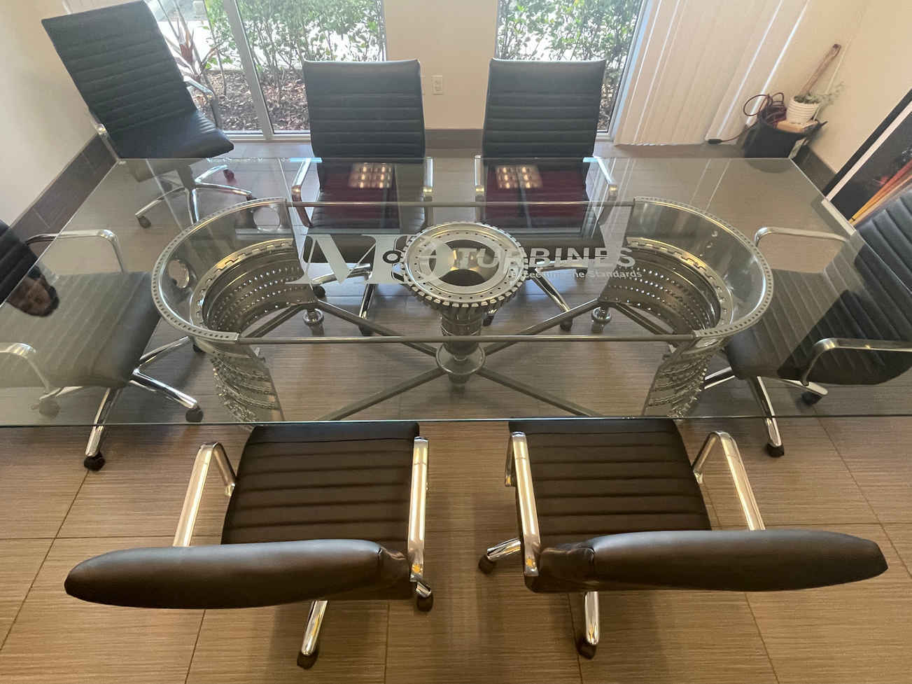 Glass conference table with metal airplane engine base, surrounded by black leather chairs.