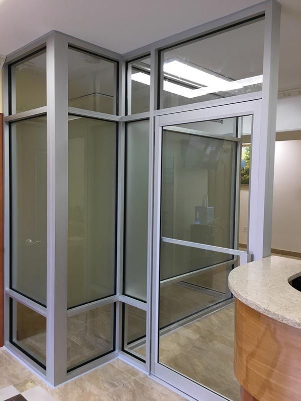Glass-walled office entryway with silver frames and a frosted glass panel; brown and beige flooring, reception desk.