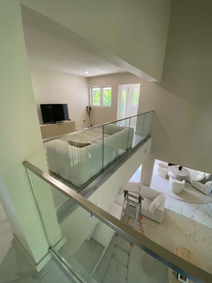 A modern living room with a loft area, white furniture, and glass railings.