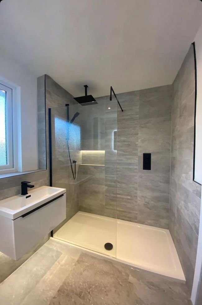 Modern bathroom with a walk-in shower, white vanity, gray tiled walls, and black fixtures.