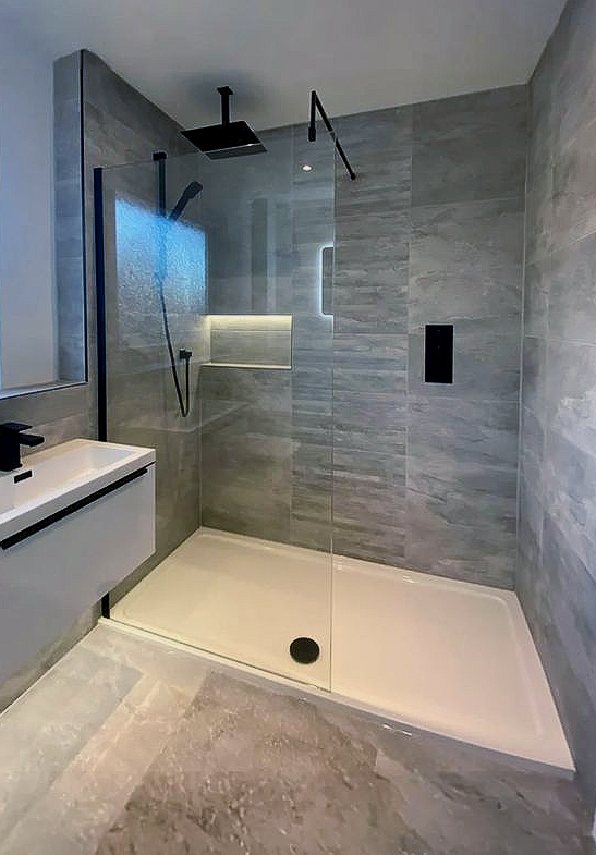 Modern bathroom with gray tiled walls, walk-in shower, black fixtures, and white vanity.