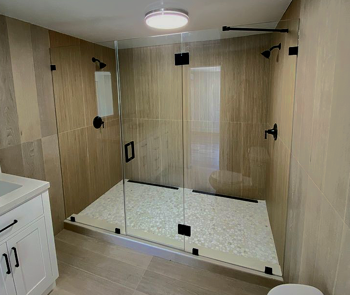 Modern bathroom with large glass shower enclosure; beige tile walls; black fixtures.
