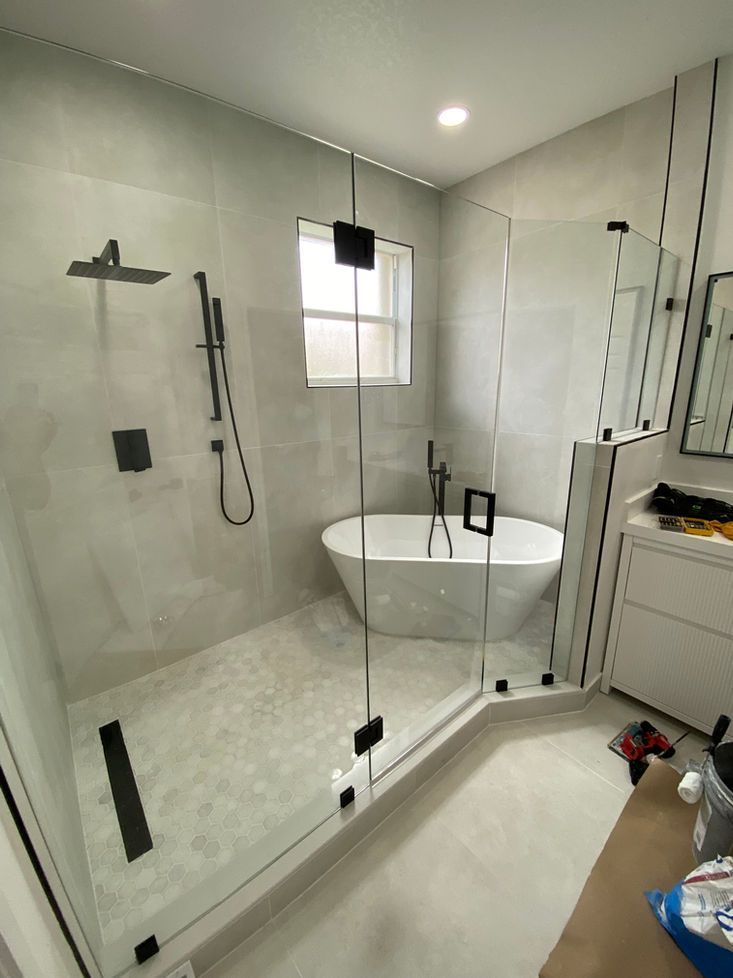Modern bathroom with a glass-enclosed shower, freestanding tub, and light gray tile walls. Black fixtures.