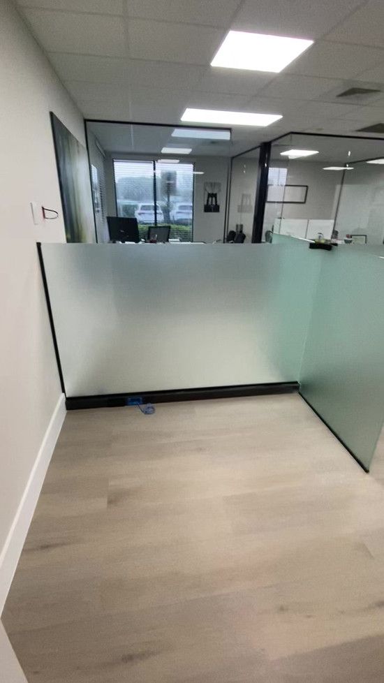 Office interior with frosted glass partitions, light wood flooring, and overhead lights.