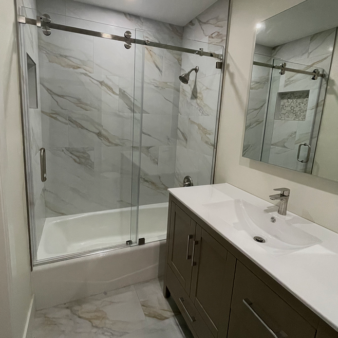 Bathroom with marble-look tile, glass shower doors, a vanity with a white sink, and a rectangular mirror.