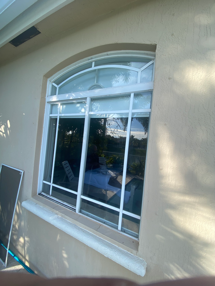 White-framed arched window with white security bars on a beige stucco wall; a window screen leans against the wall nearby.