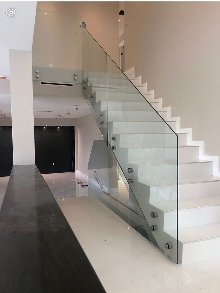 Modern staircase with glass railing. White steps, light walls, and shiny floor.