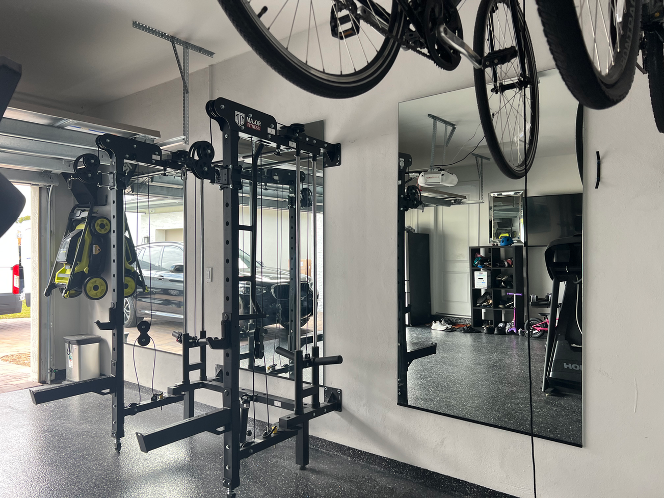 Garage gym with mirrors, weight racks, and hanging bicycles.