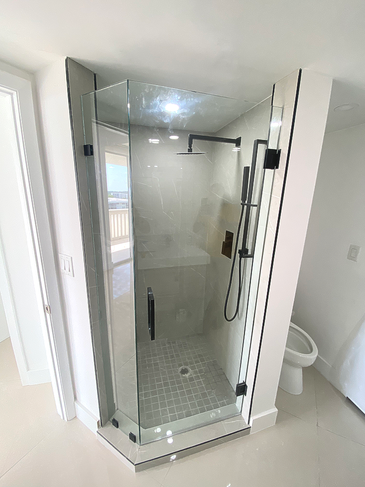 Glass shower with black fixtures and gray tile inside a white bathroom.