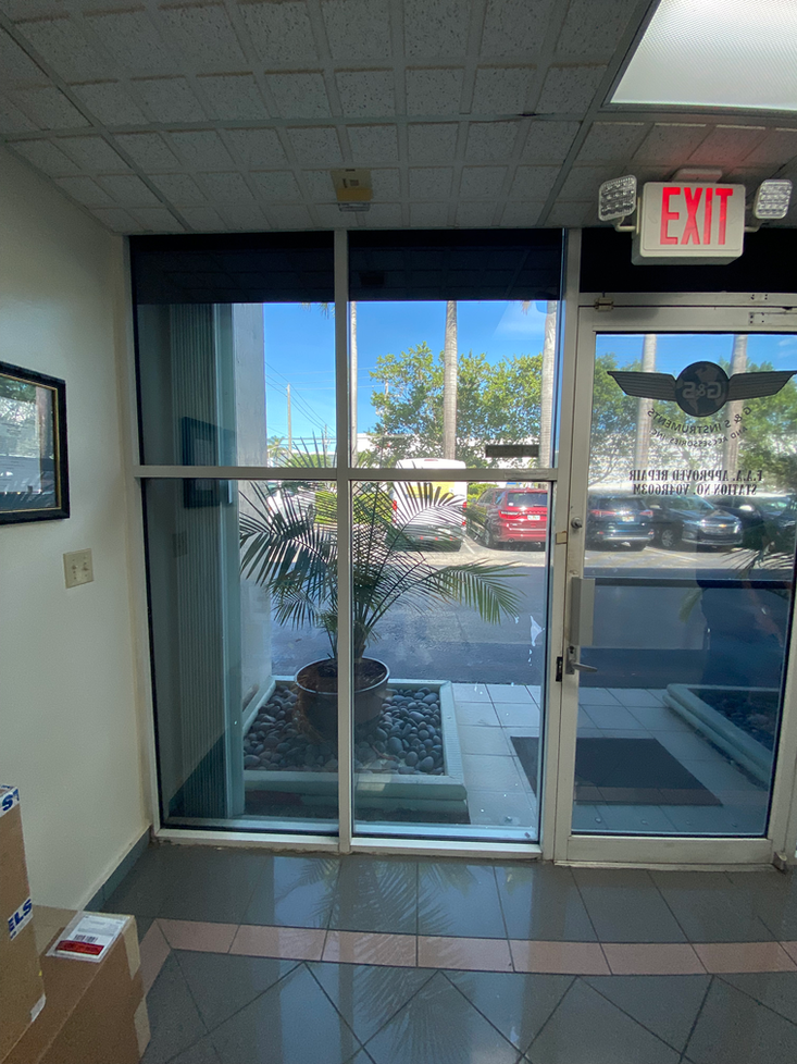 View of an interior door with an exit sign. Through the glass, cars and plants are visible outside.