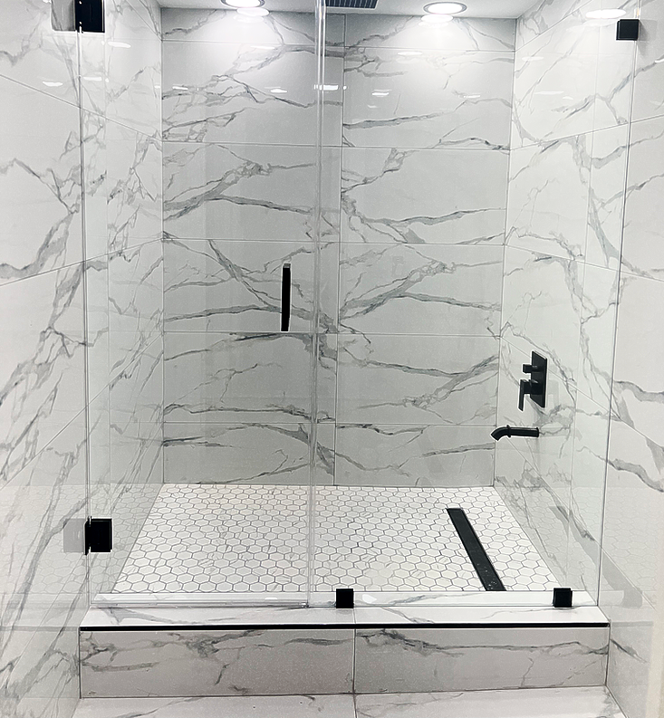 Marble-tiled shower with clear glass doors and black fixtures, featuring a penny tile floor and overhead shower head.
