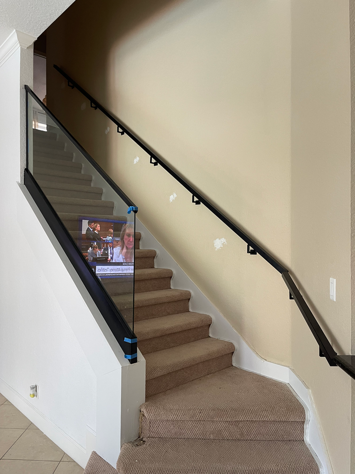 Staircase with glass railing and black handrail, tan carpet, and beige walls.