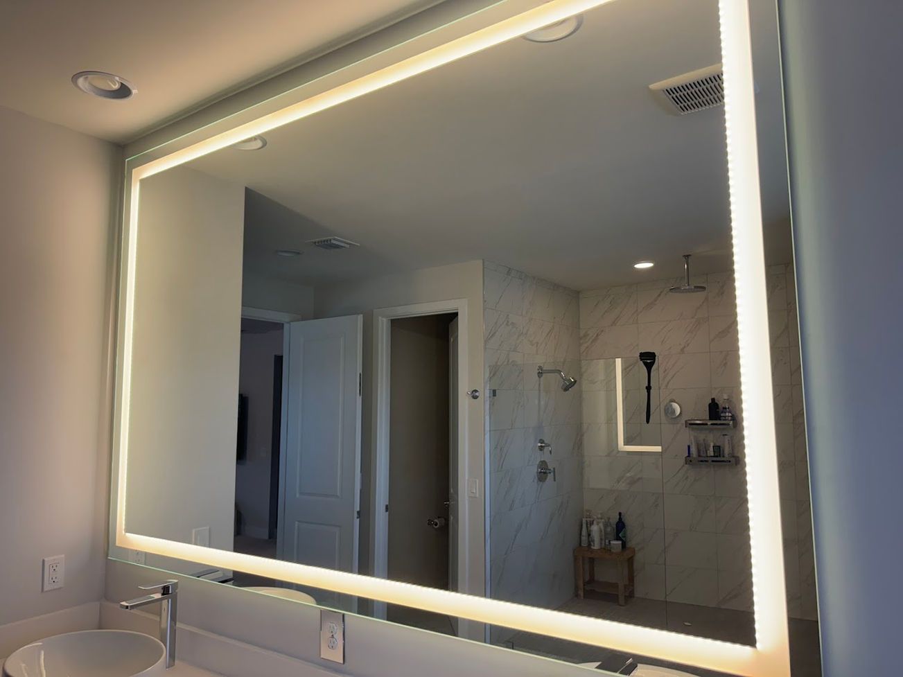 Large rectangular mirror with surrounding LED lighting in a bathroom, reflecting the shower and sink.