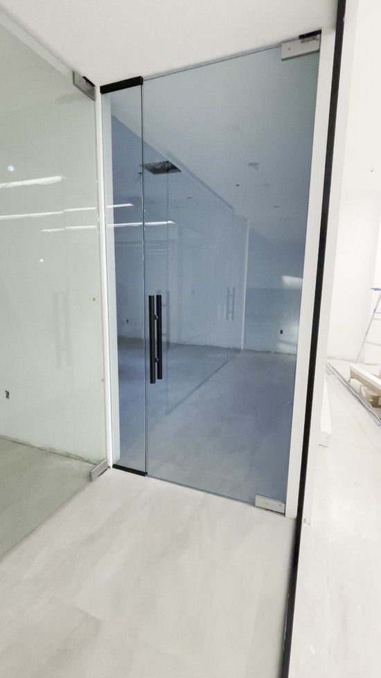 Glass door with black handle leading into an empty room with white walls and gray floor.