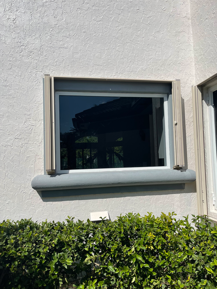 Window with dark tint and gray trim set into a white stucco wall, with tan sunshades retracted.
